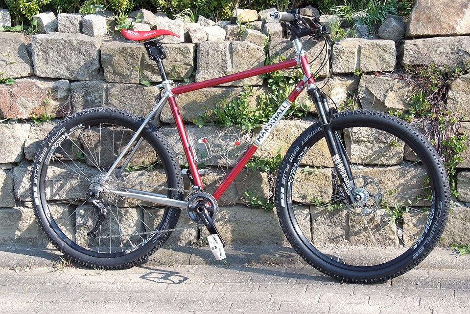 Rotes Marschall-Mountainbike mit poliertem Edelstahl-Hinterbau vor einer Natursteinmauer