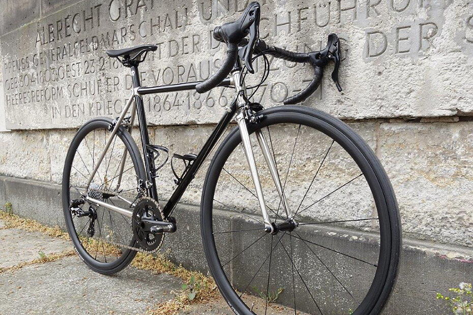 Schwarz-silbernes Marschall-Rennrad mit Edelstahl-Muffen vor einem Steinrelief