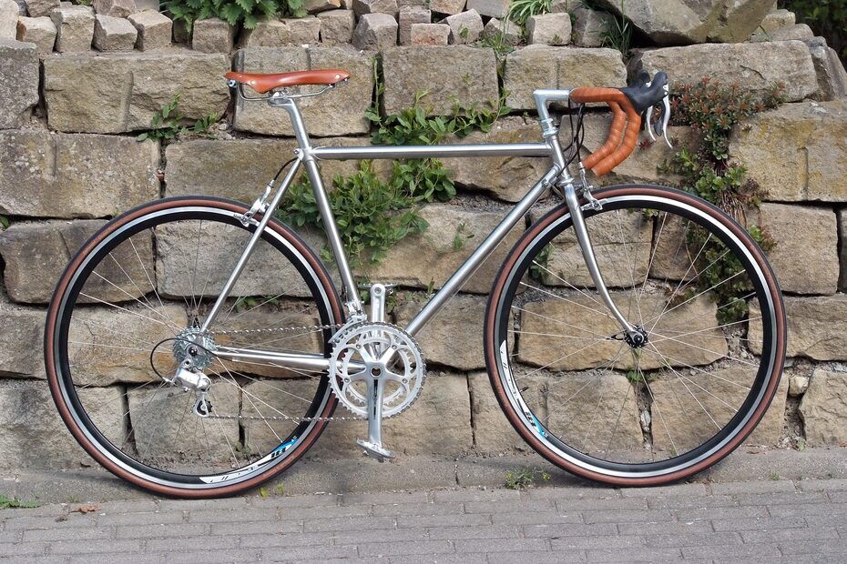 Marschall-Randonneur aus Edelstahl mit braunem Ledersattel und passendem Lenkerband vor einer Natursteinmauer