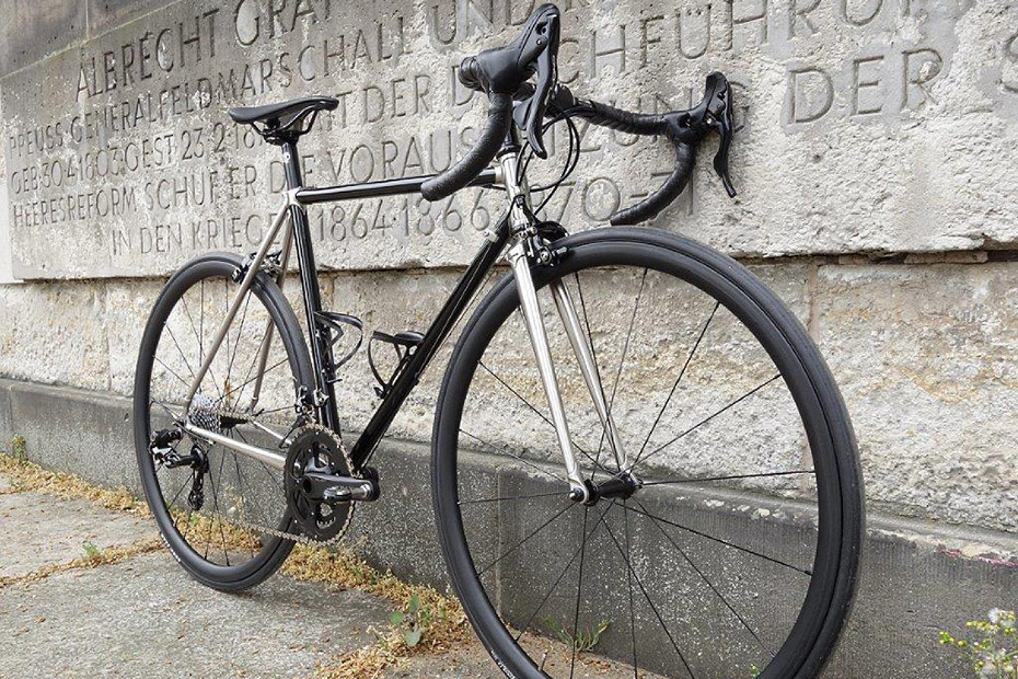 Schwarz-silbernes Marschall-Rennrad mit Edelstahl-Muffen vor einem Steinrelief